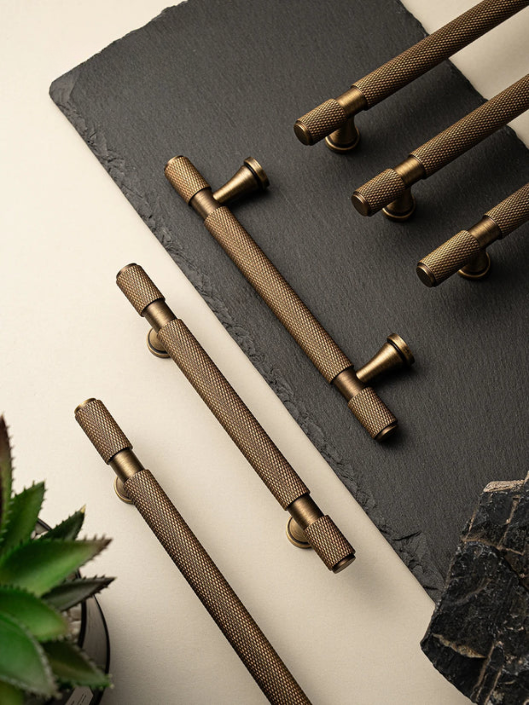 Set of bronze cabinet handles on a dark surface with a plant in the corner.