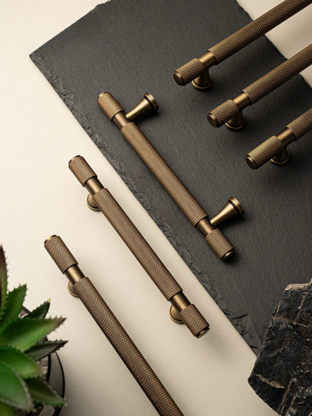 Set of bronze cabinet handles on a dark surface with a plant in the corner.