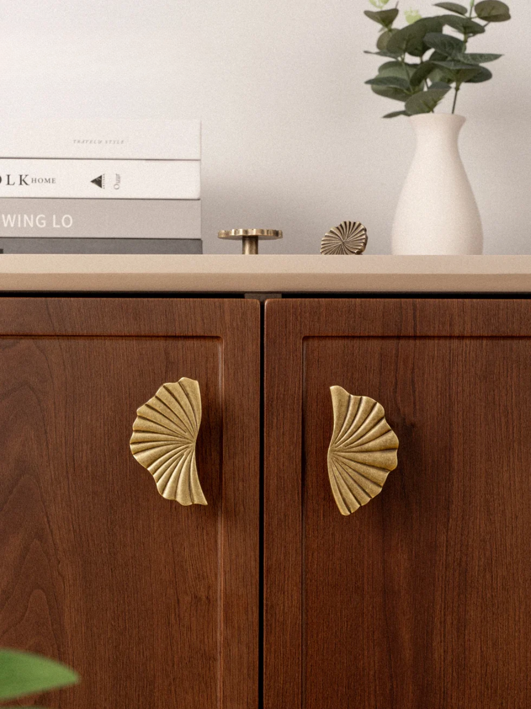 Wooden cabinet with shell-shaped brass handles on a neutral background