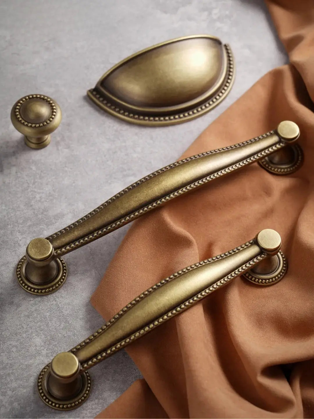 Set of brass cabinet handles and knobs on a textured surface with fabric.