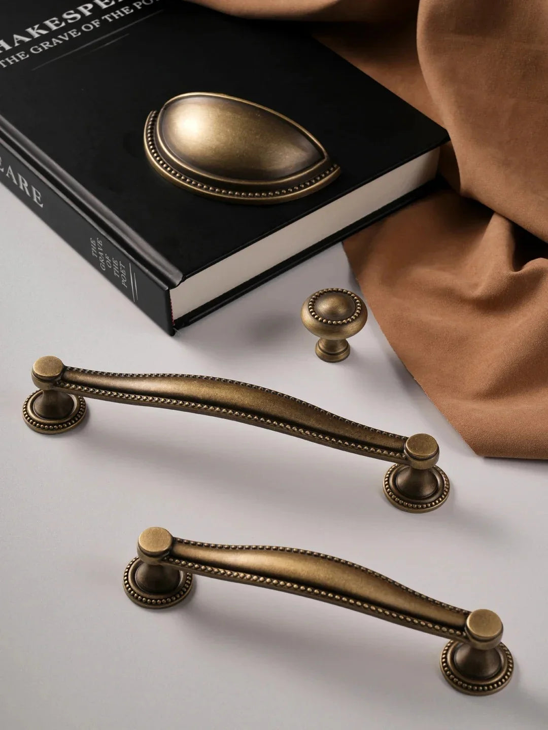 Set of bronze cabinet handles on a white surface with a book in the background