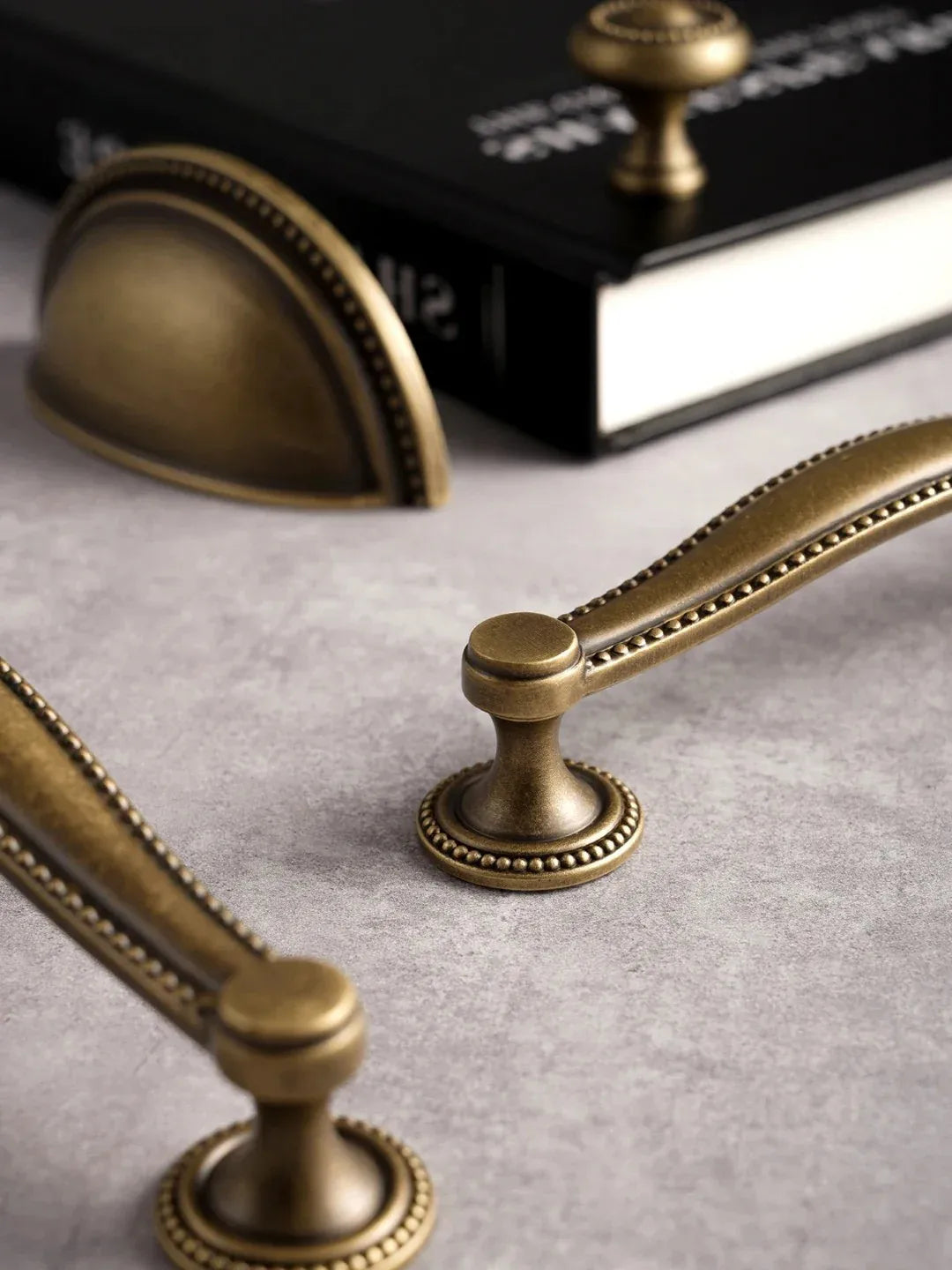 Close-up of vintage-style brass cabinet handles on a textured surface with a book in the background.