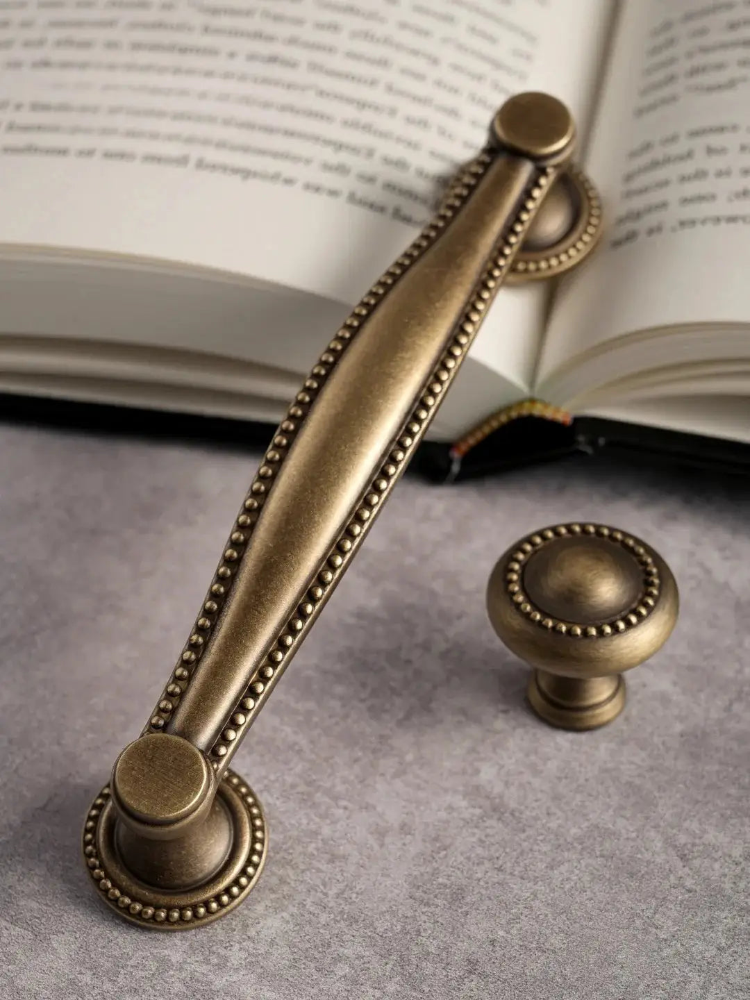 Bronze cabinet handle and knob set on a textured surface with an open book in the background.