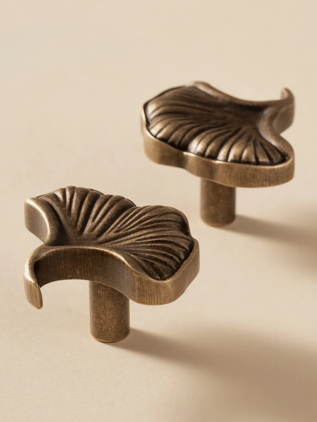 Two bronze leaf-shaped cabinet knobs on a beige background