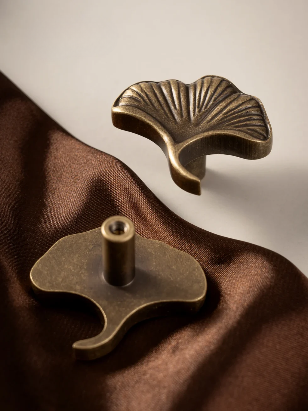 Two brass leaf-shaped objects on a brown fabric background