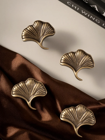 Four gold leaf-shaped earrings on a brown fabric background