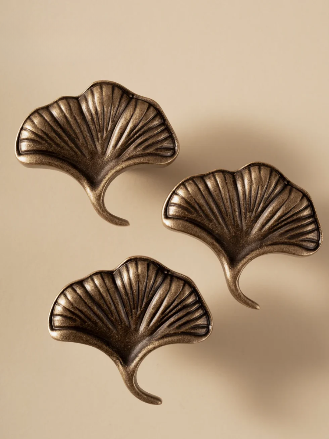 Three bronze leaf-shaped wall hooks on a beige background