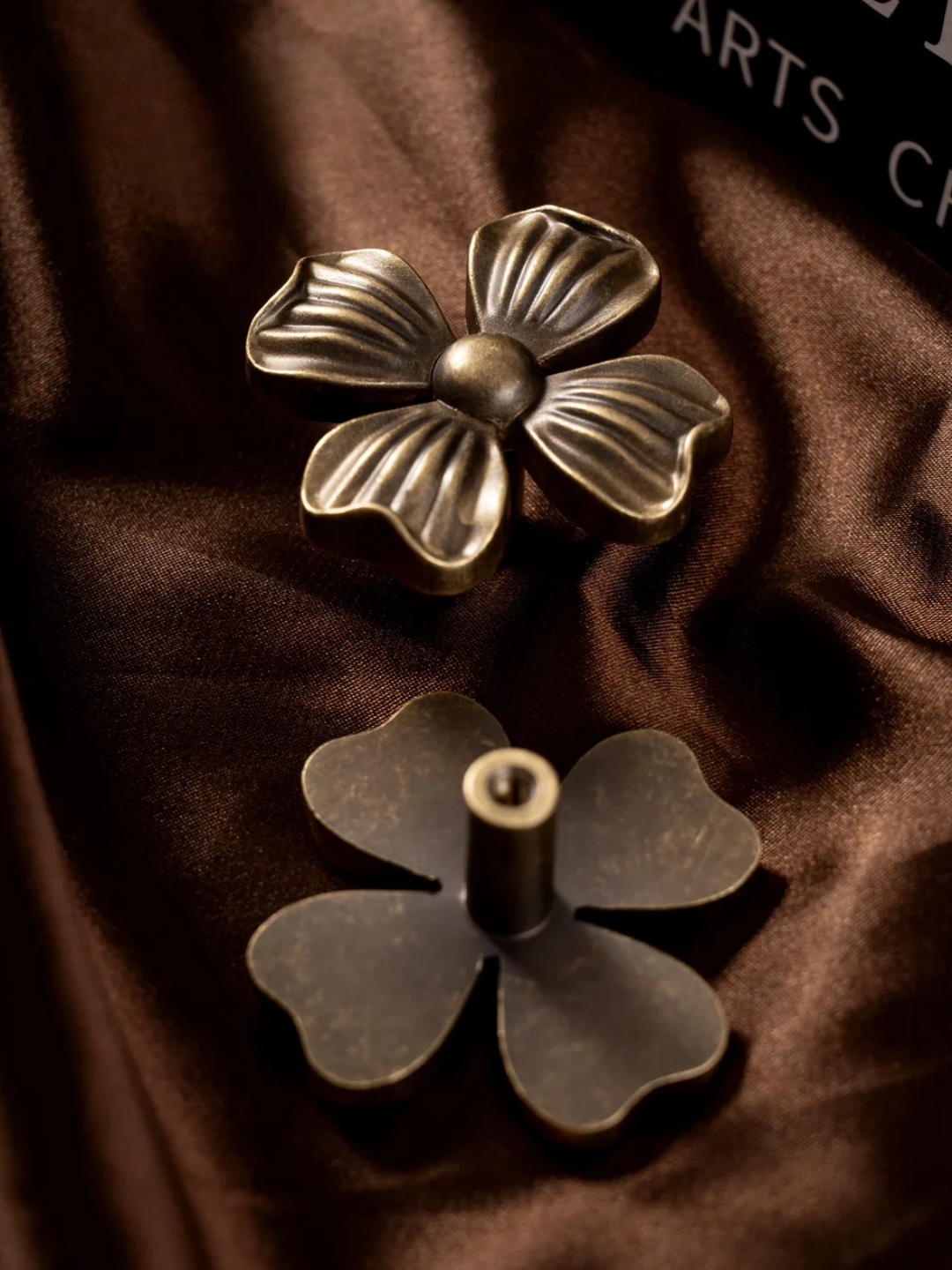 Two bronze flower-shaped objects on a brown fabric background