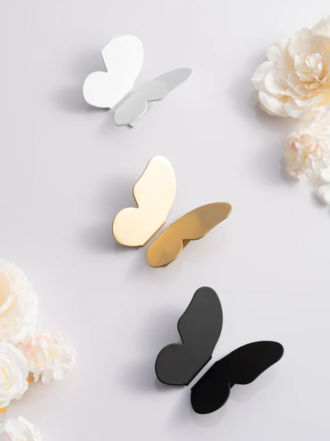 Butterfly-shaped earrings in gold, silver, and black on a light background with flowers.