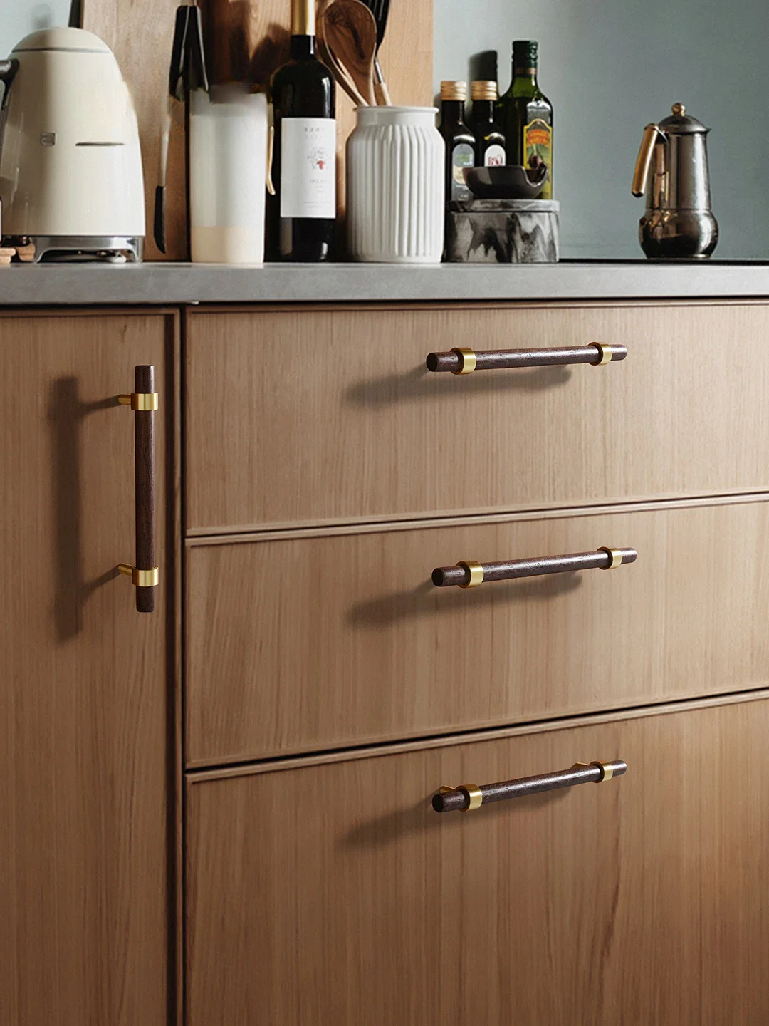 Wooden kitchen cabinets with dark handles on a countertop with kitchen items.