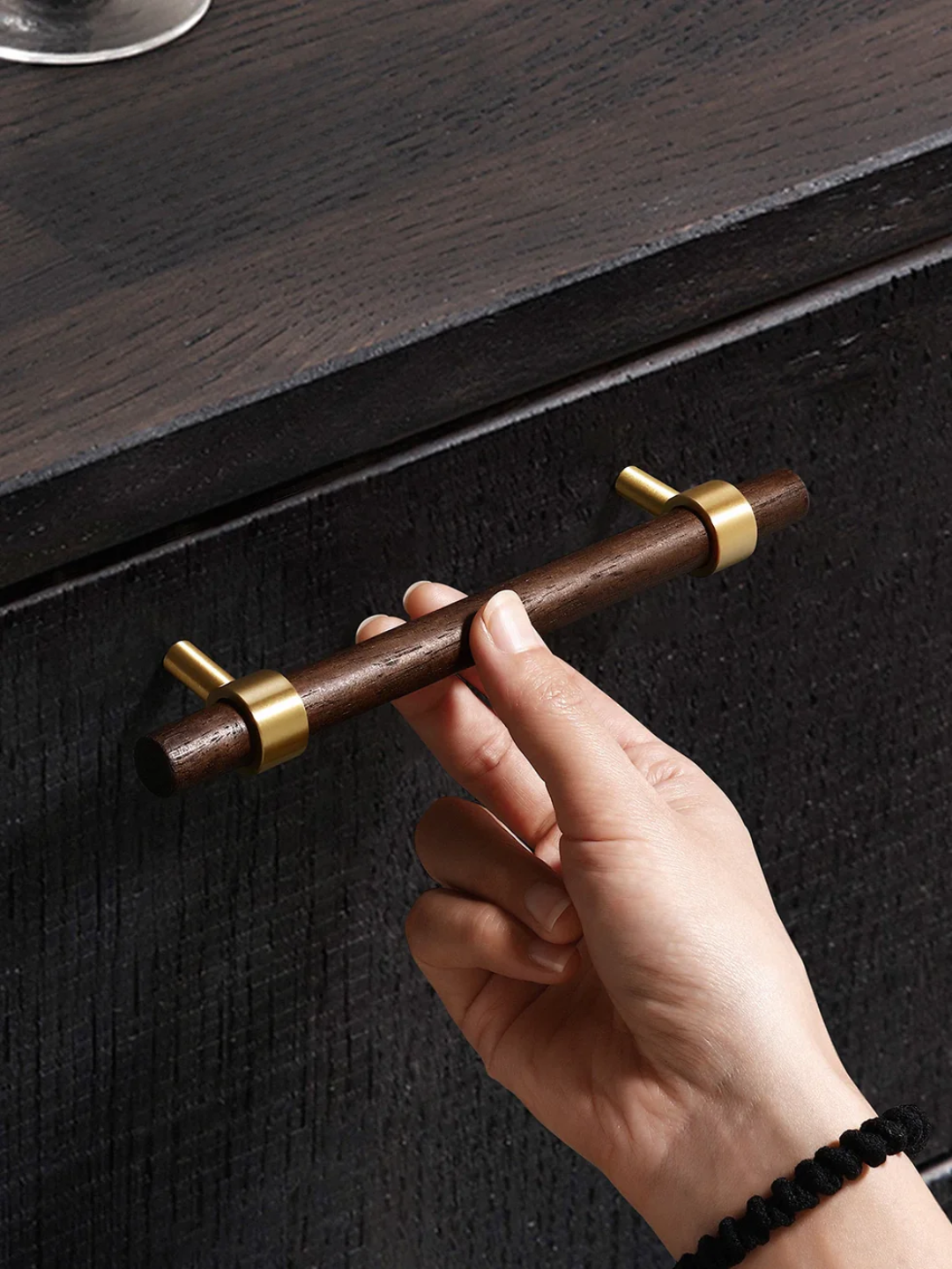 Hand holding a wooden drawer handle with gold accents on a dark wooden surface