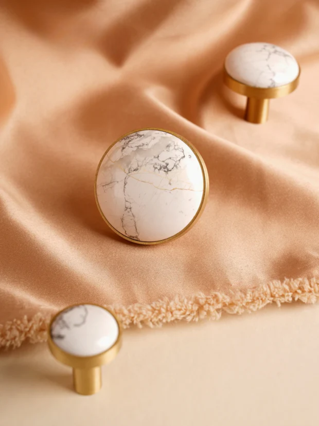 Decorative knobs with marble pattern and gold accents on a beige fabric background