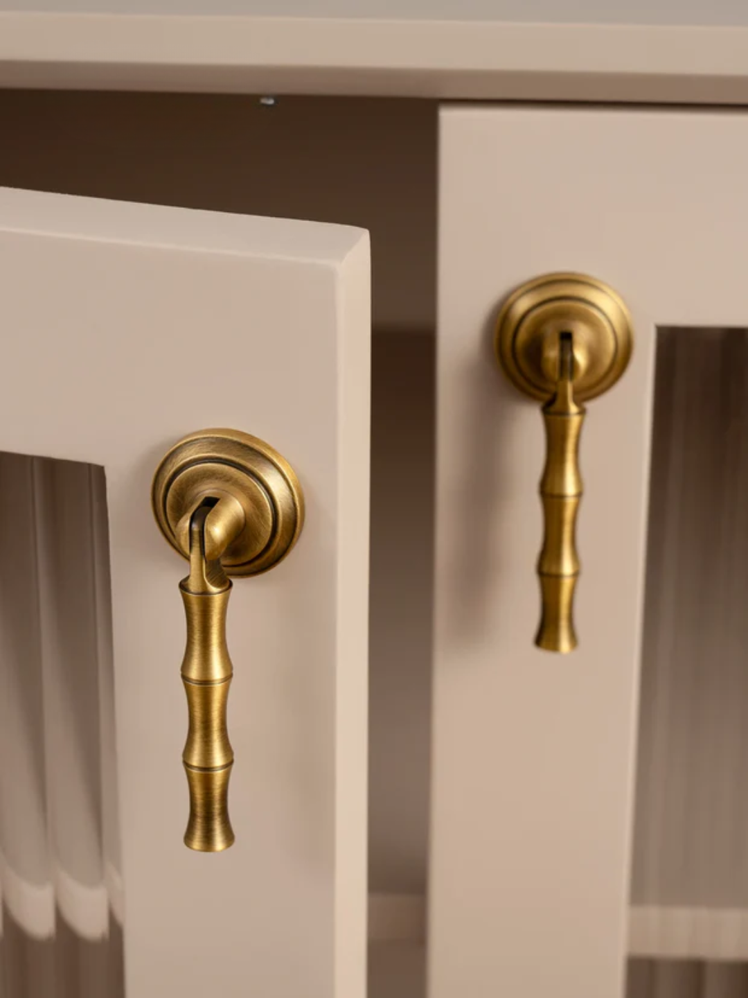 Close-up of two gold cabinet handles on a neutral-colored cabinet.