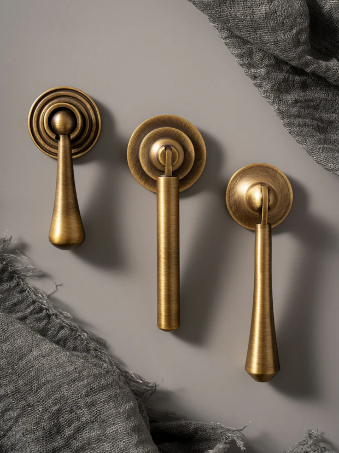 Three brass door handles on a gray surface with textured fabric.