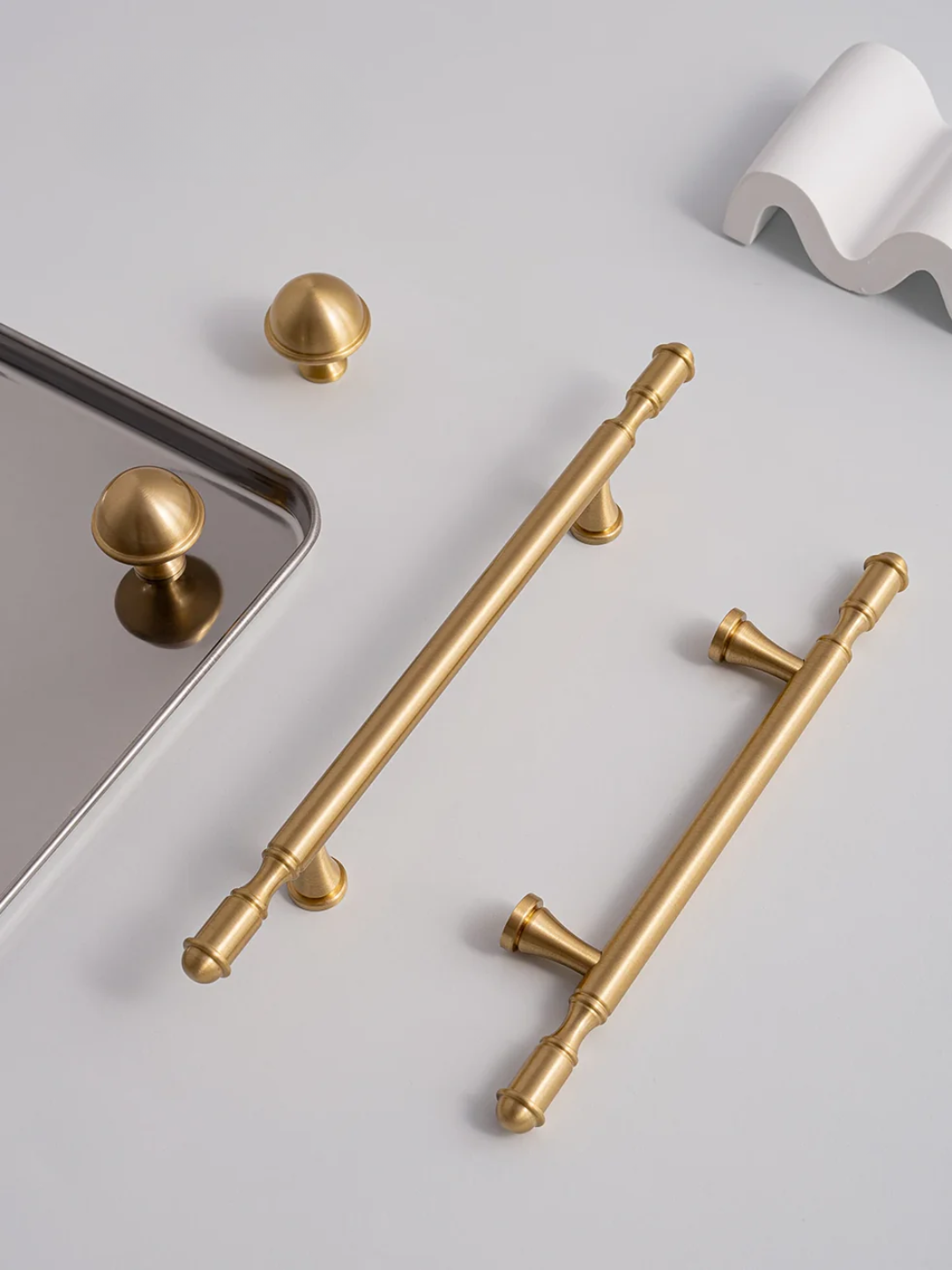 Gold cabinet handles on a white surface with a white decorative object in the background.