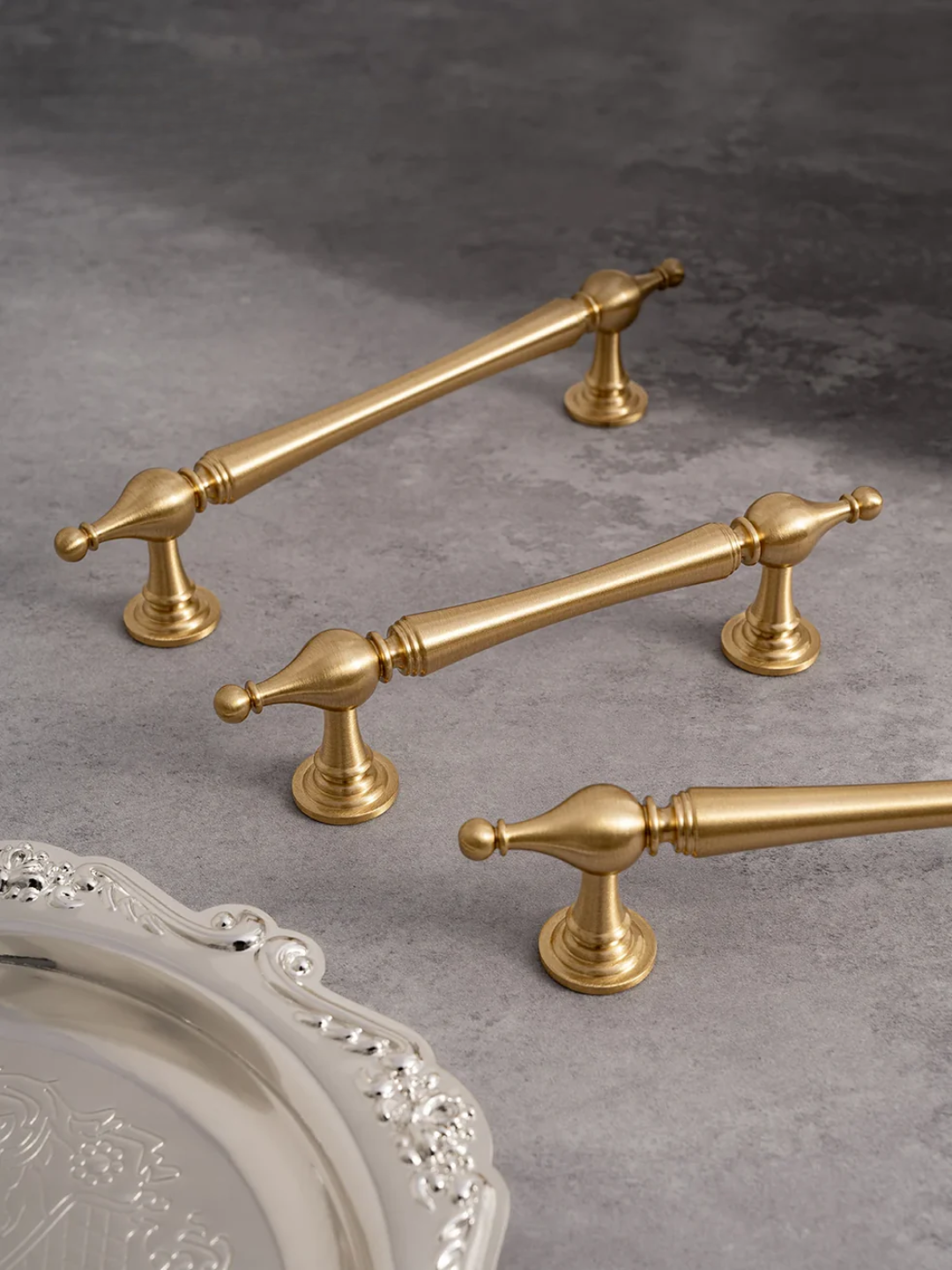 Gold cabinet handles on a gray surface with a decorative tray.