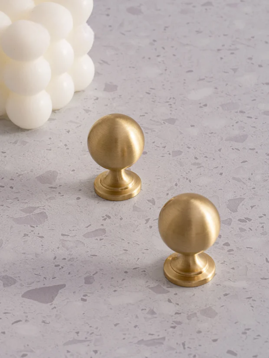 Two gold cabinet knobs on a gray surface with white decorative elements.