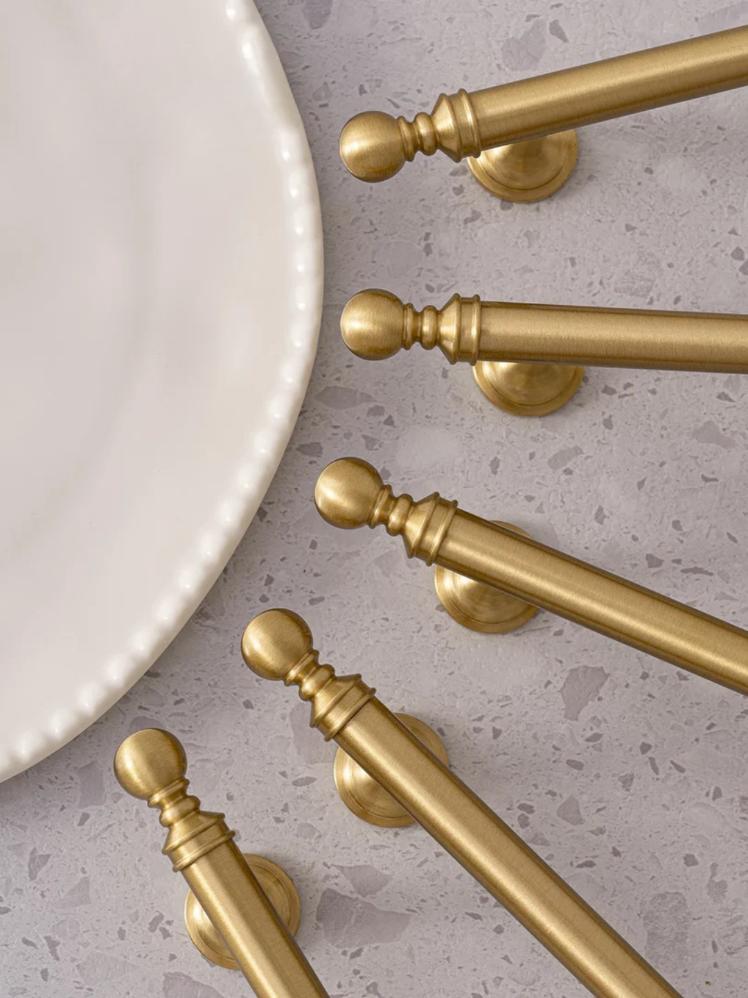 Set of gold cabinet handles on a white plate against a gray background