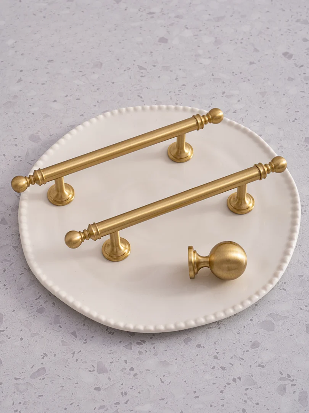 Set of gold cabinet handles on a white plate against a gray background