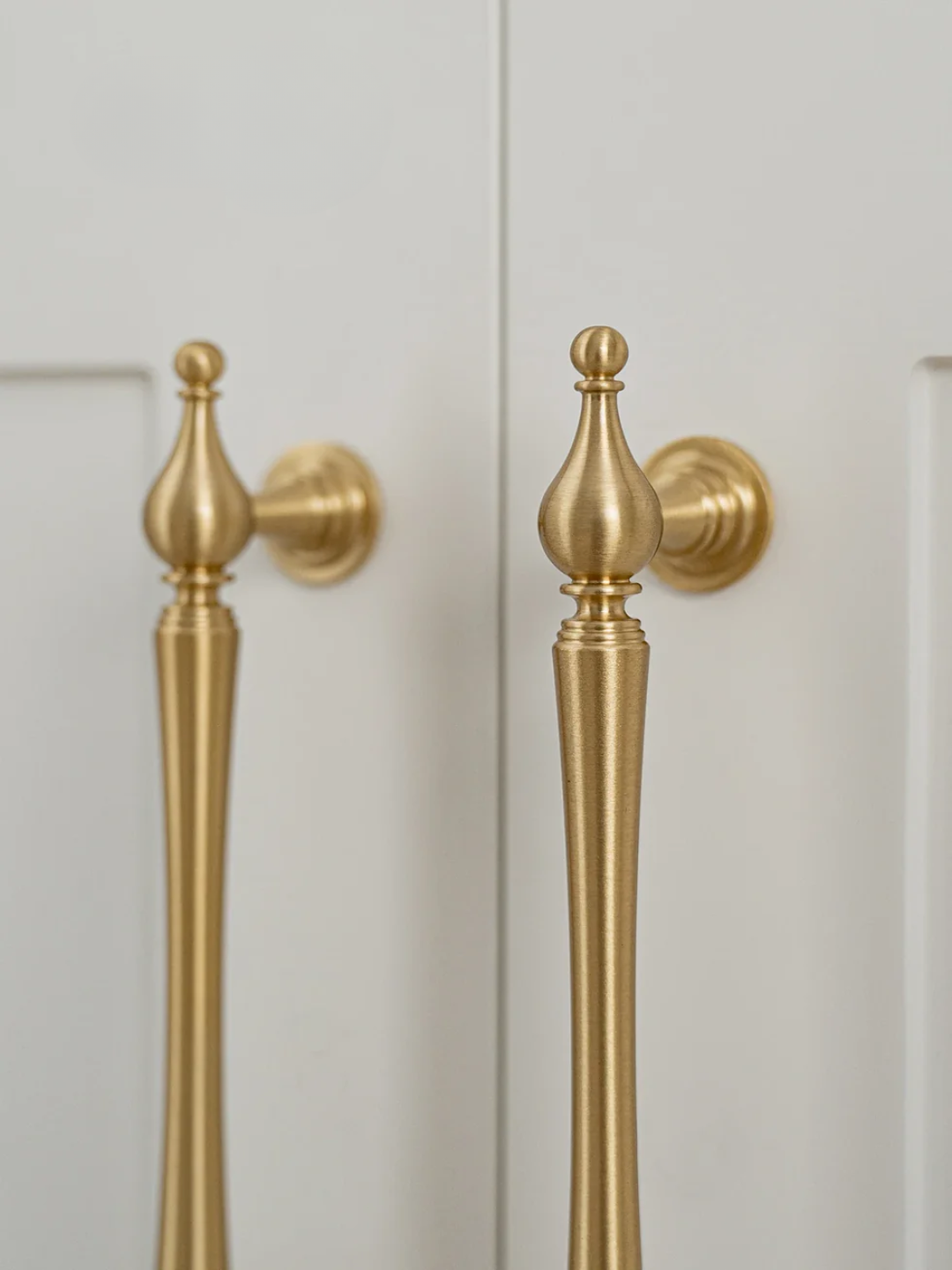 Close-up of gold cabinet handles on a light-colored cabinet door.