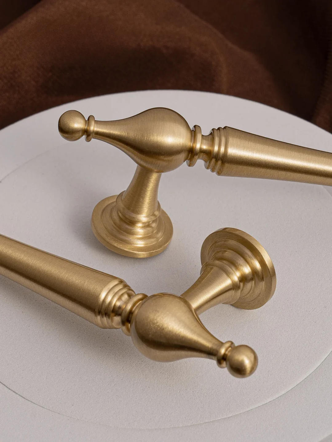 Two gold towel bars on a white surface with a brown fabric background