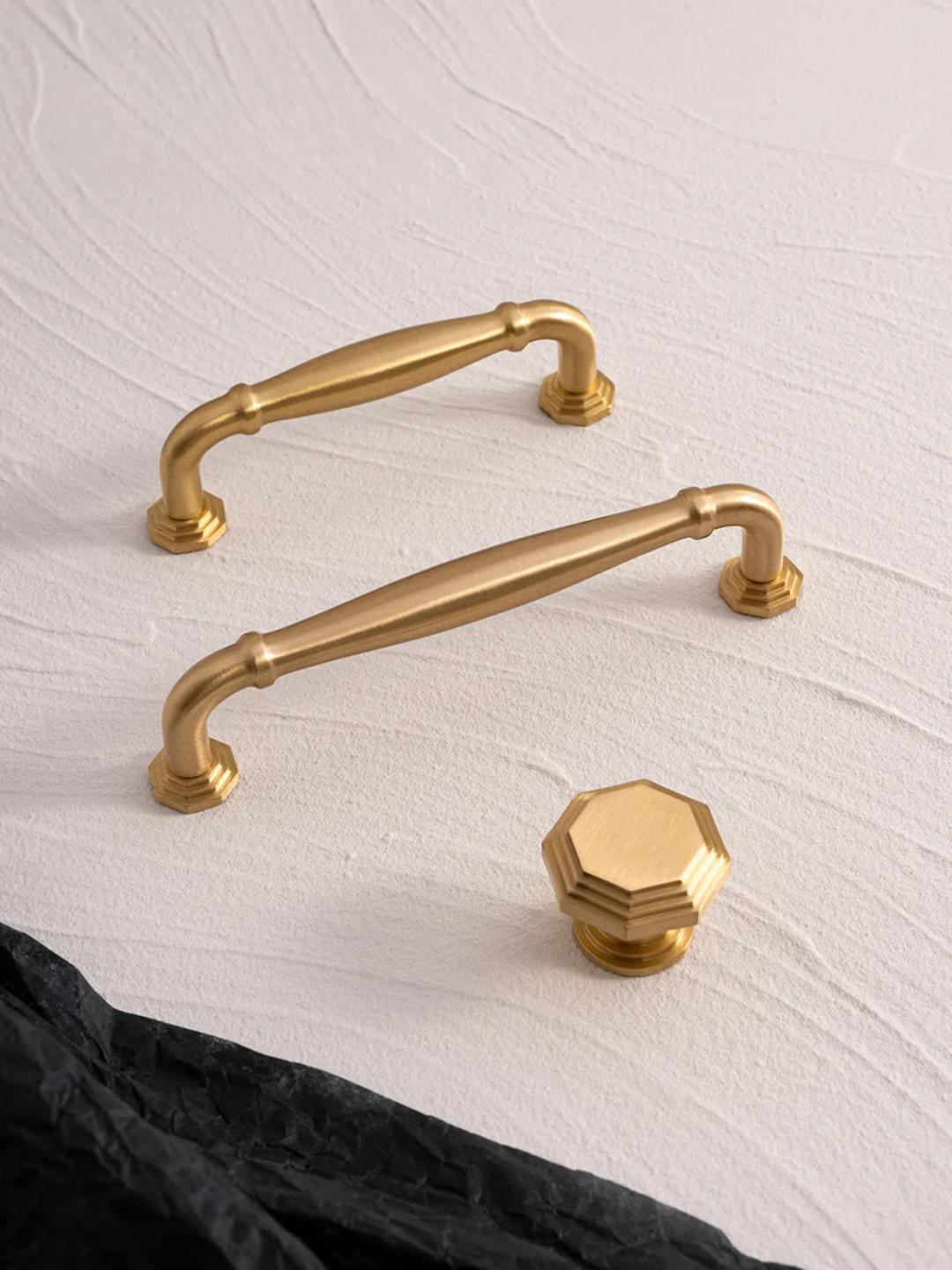 Gold cabinet handles and a hexagonal knob on a textured white surface
