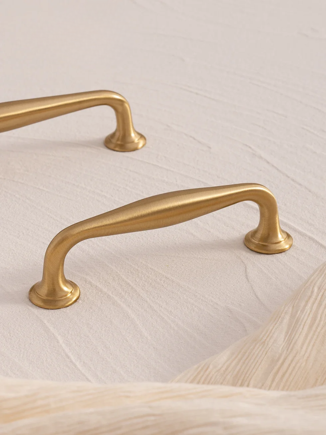 Two gold cabinet handles on a light wood surface