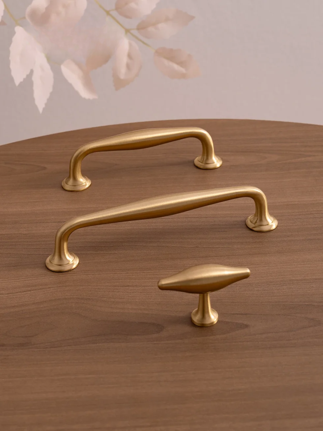 Three gold cabinet handles on a wooden surface with a soft pink floral background.