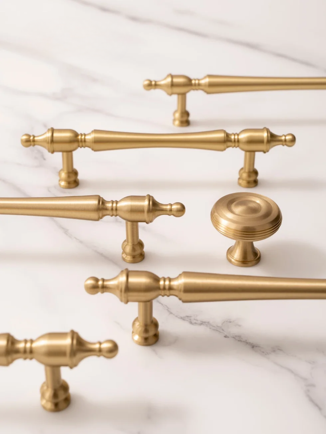 Collection of gold cabinet handles and knobs on a marble surface
