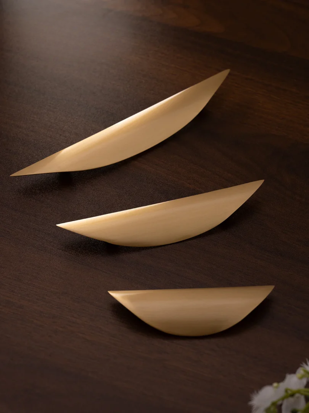 Set of gold leaf-shaped objects on a wooden surface with white flowers in the corner.