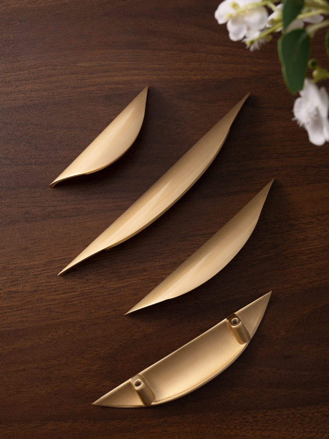 Set of gold leaf-shaped objects on a wooden surface with white flowers in the corner.