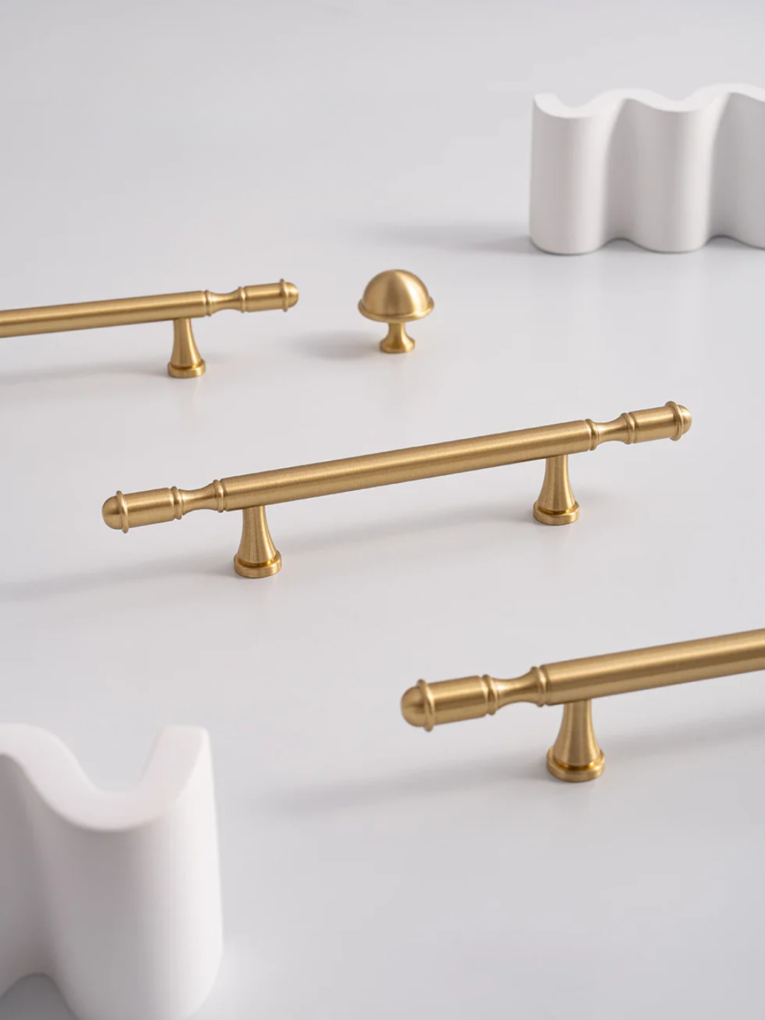 Gold cabinet handles on a white surface with a white decorative object in the background.