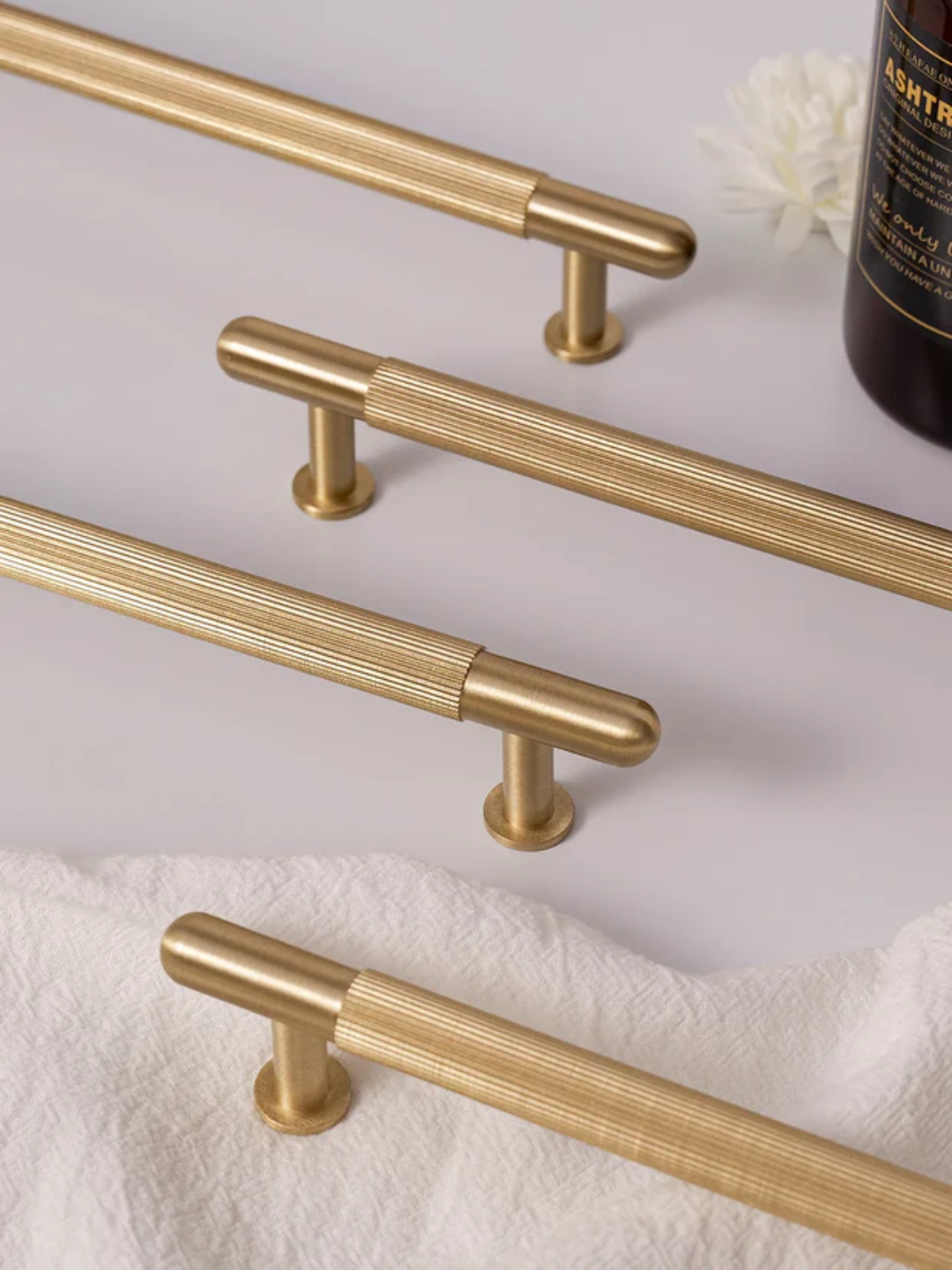 Set of gold cabinet handles on a white surface with a bottle in the background