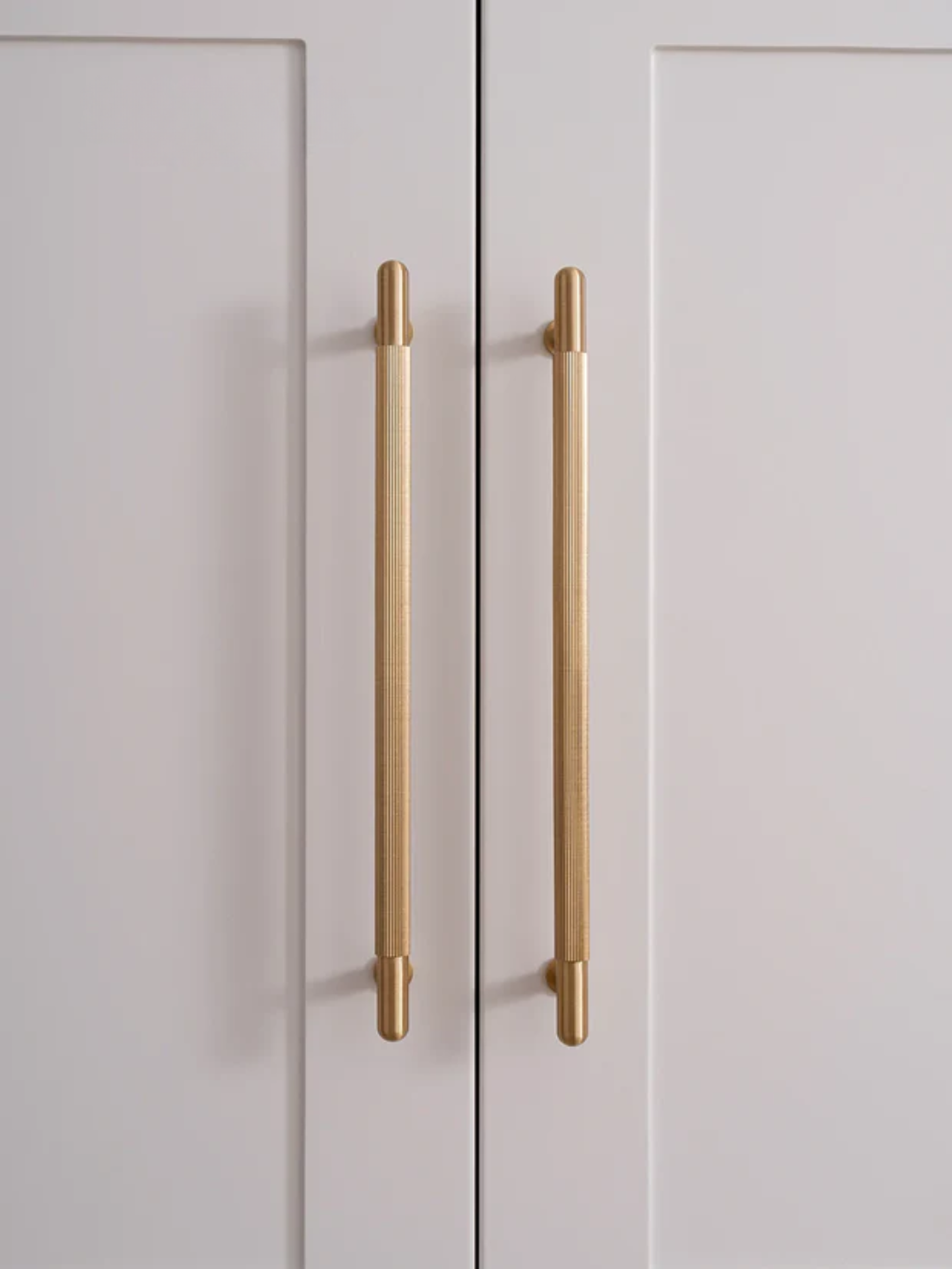 Close-up of two gold cabinet handles on a white door