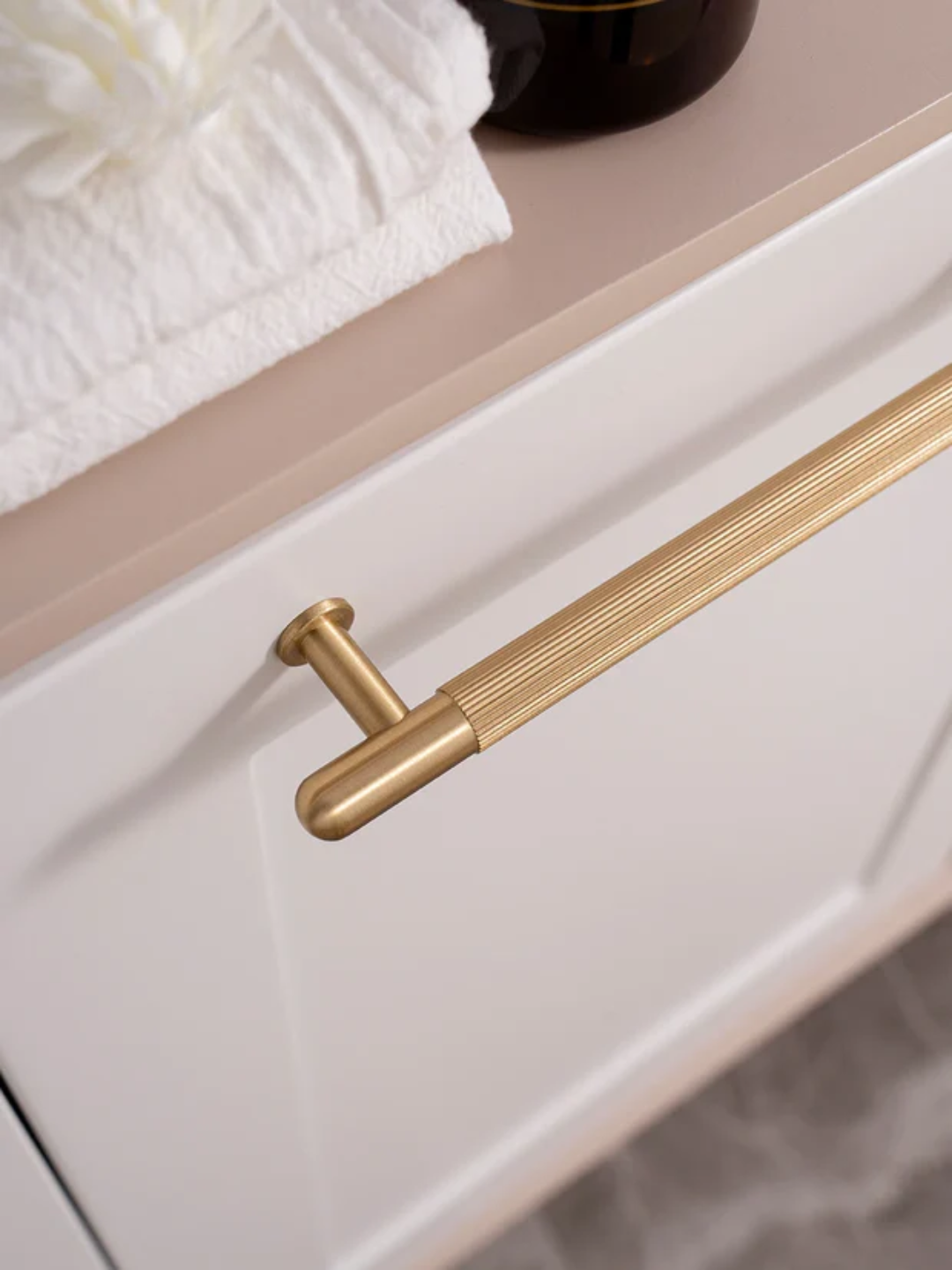 Close-up of a gold cabinet handle on a white cabinet with a neutral background