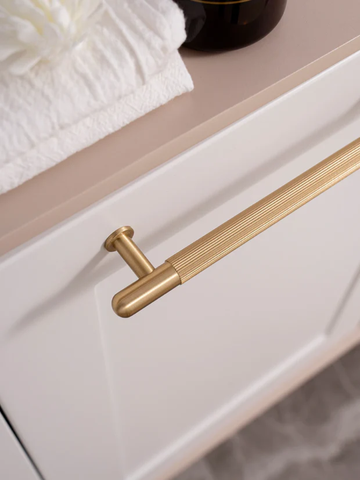 Close-up of a gold cabinet handle on a white cabinet with a neutral background