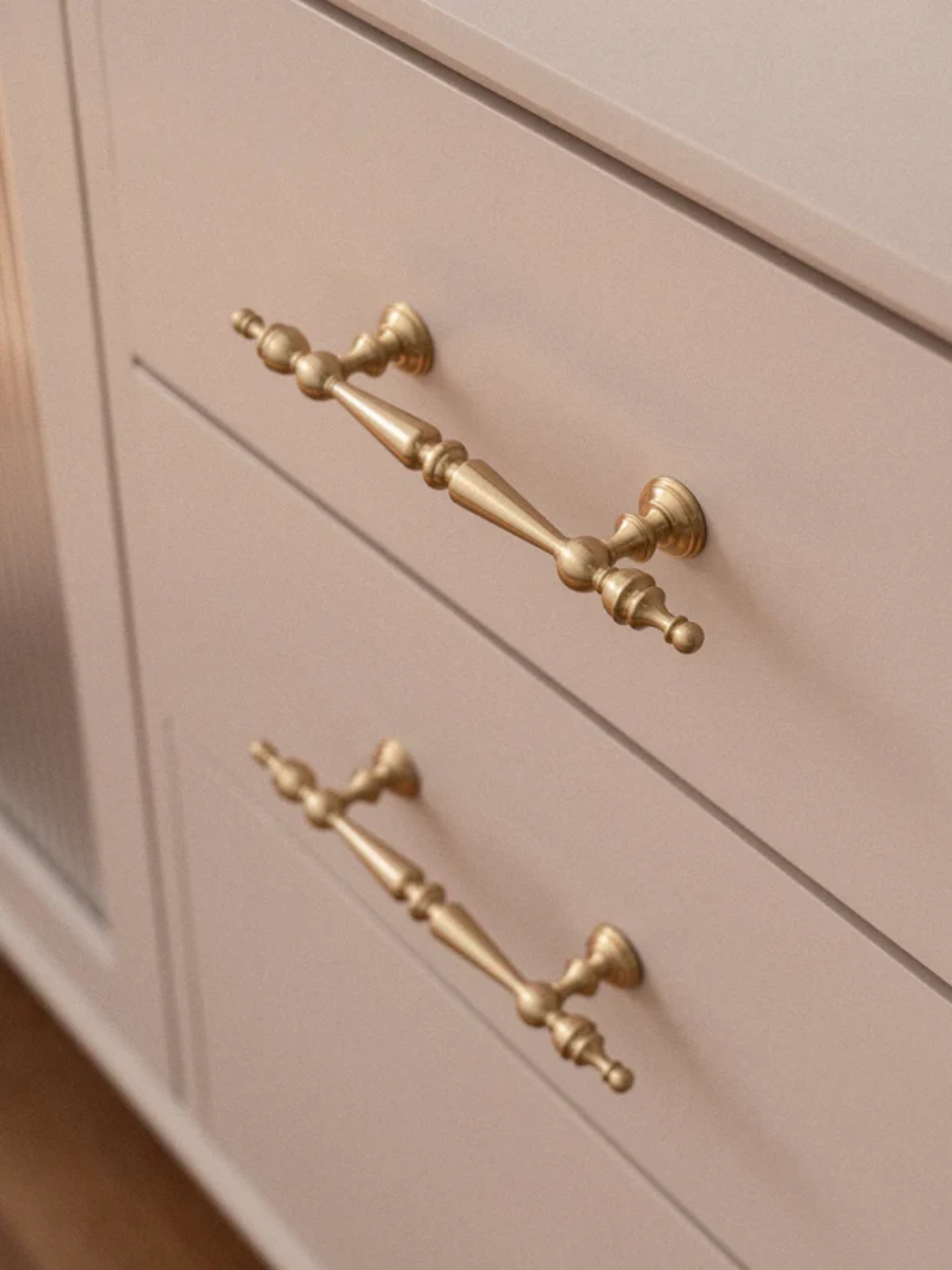 Close-up of a cabinet with gold handles on a light-colored wooden surface.