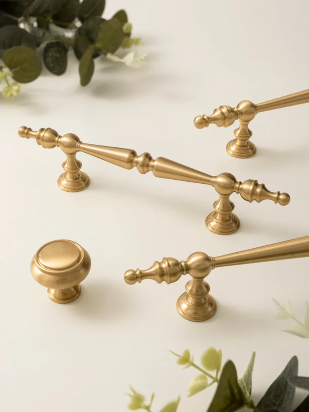 Set of gold cabinet handles and knobs on a light background with greenery.