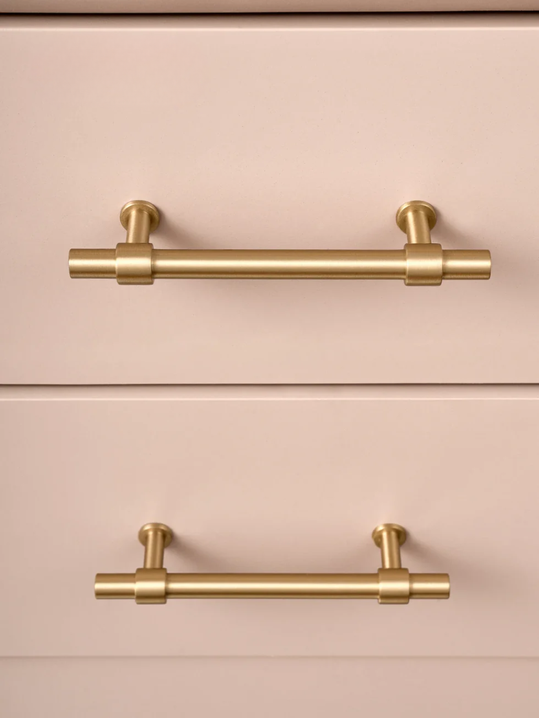 Two gold cabinet handles on a pink drawer