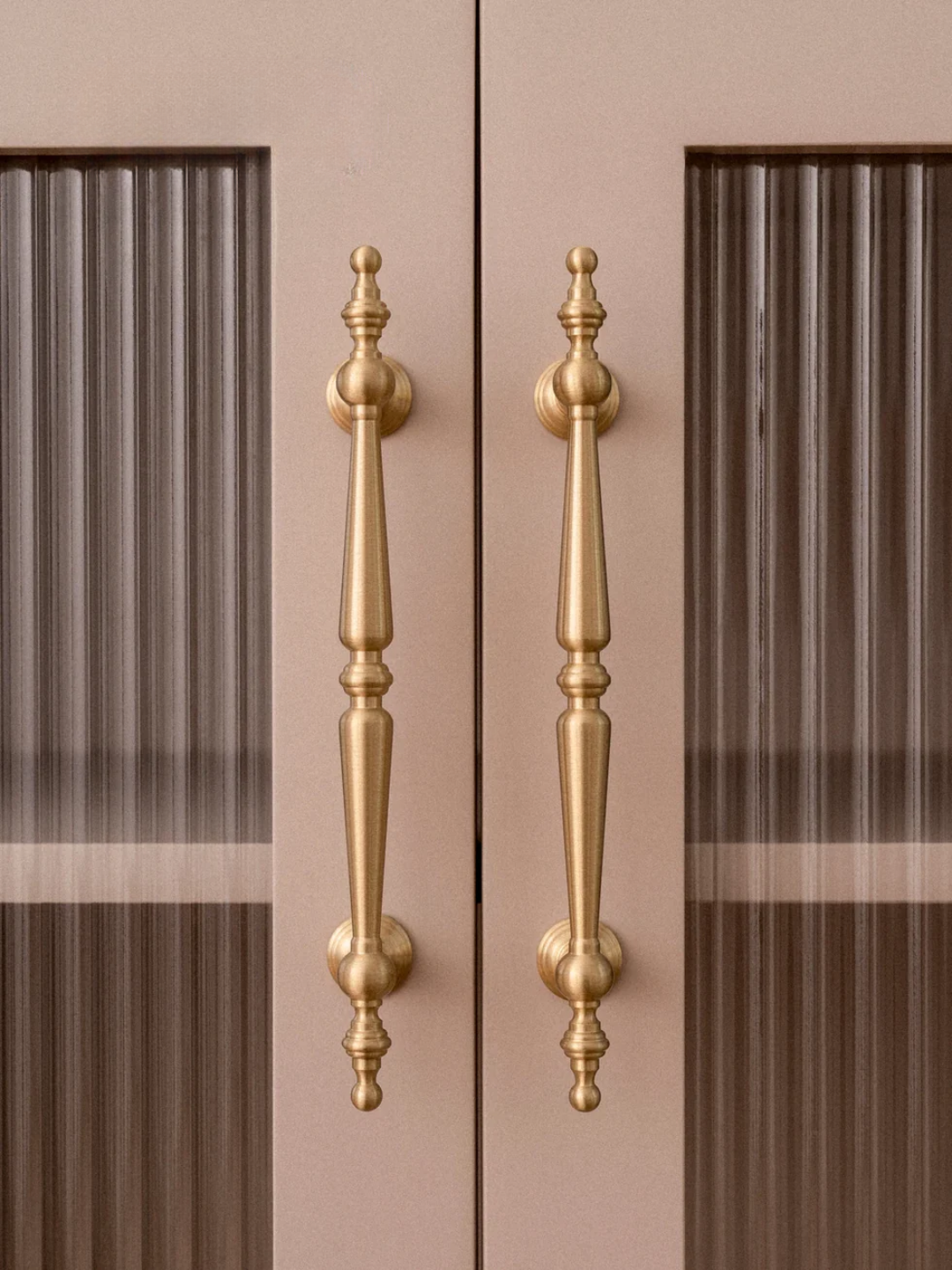 Gold cabinet handles on a brown cabinet door with a blurred background