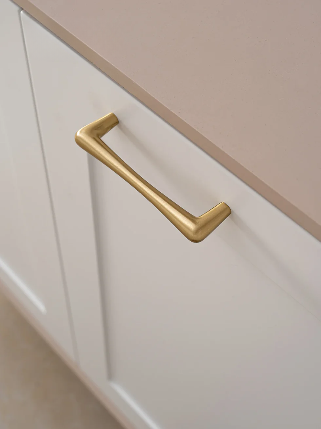 Gold cabinet handle on a white and beige cabinet