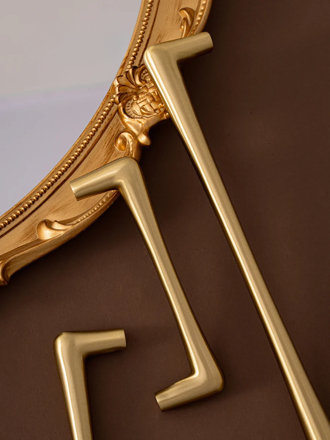 Decorative gold mirror with intricate details on a brown background.