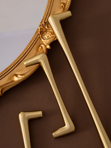 Decorative gold mirror with intricate details on a brown background.