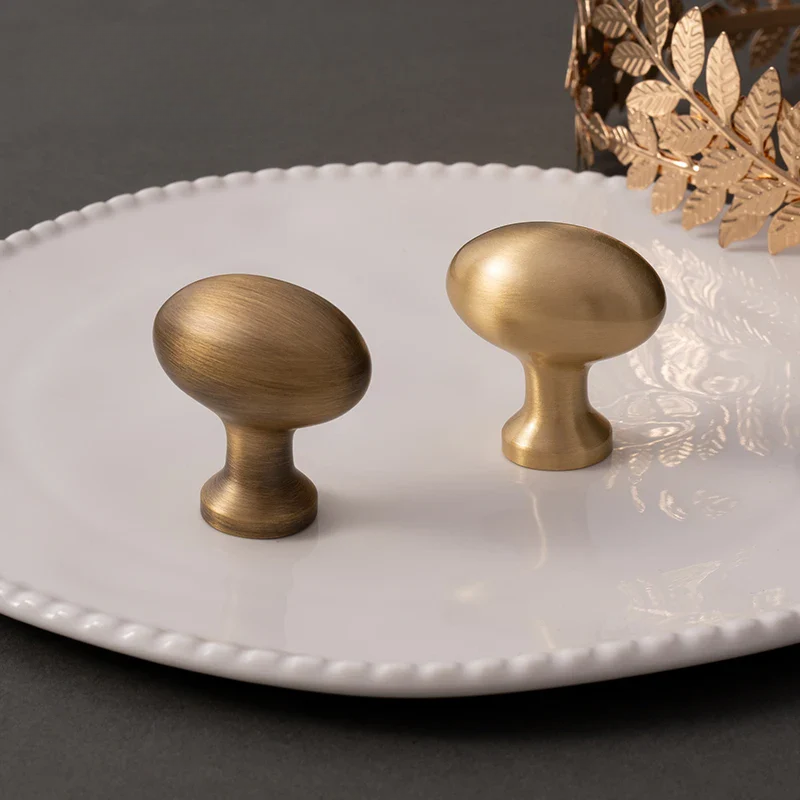 Two brass cabinet knobs on a white plate with a decorative leafy object.