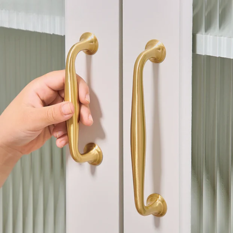 Hand holding a gold door handle on a white door with curtains in the background