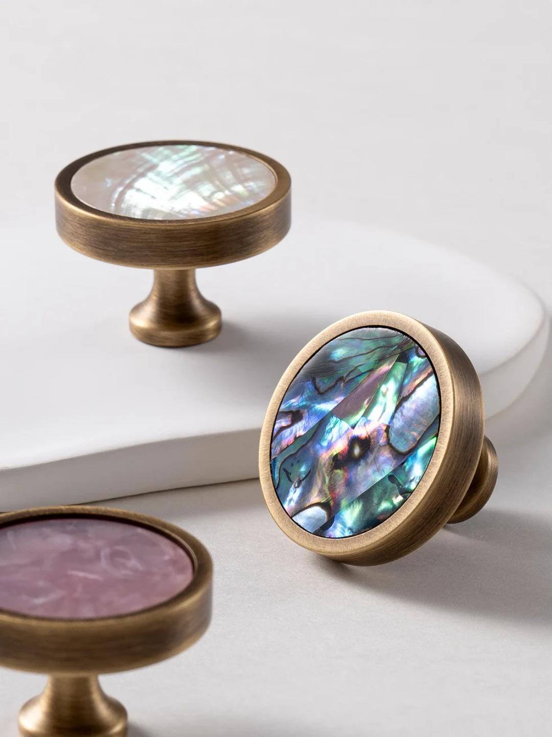 Brass cabinet knobs with natural shell inlay on a white surface, featuring the Santaya brand.