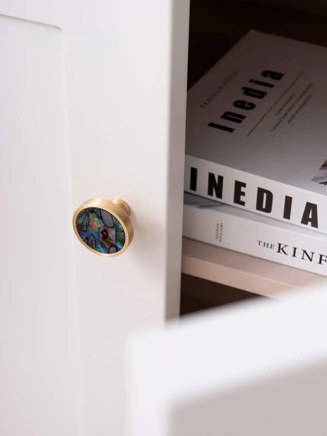 Close-up of a white cabinet with a decorative knob, open to reveal books titled 'INedia' and 'The King'.
