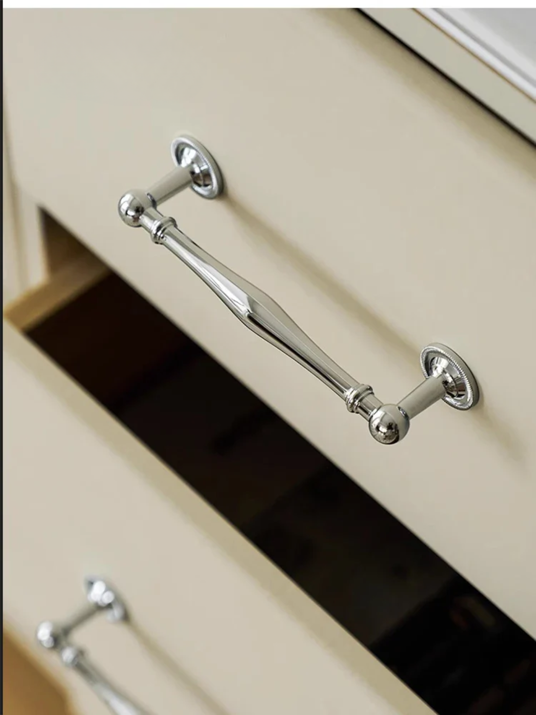 Close-up of a metallic drawer handle on a beige cabinet.