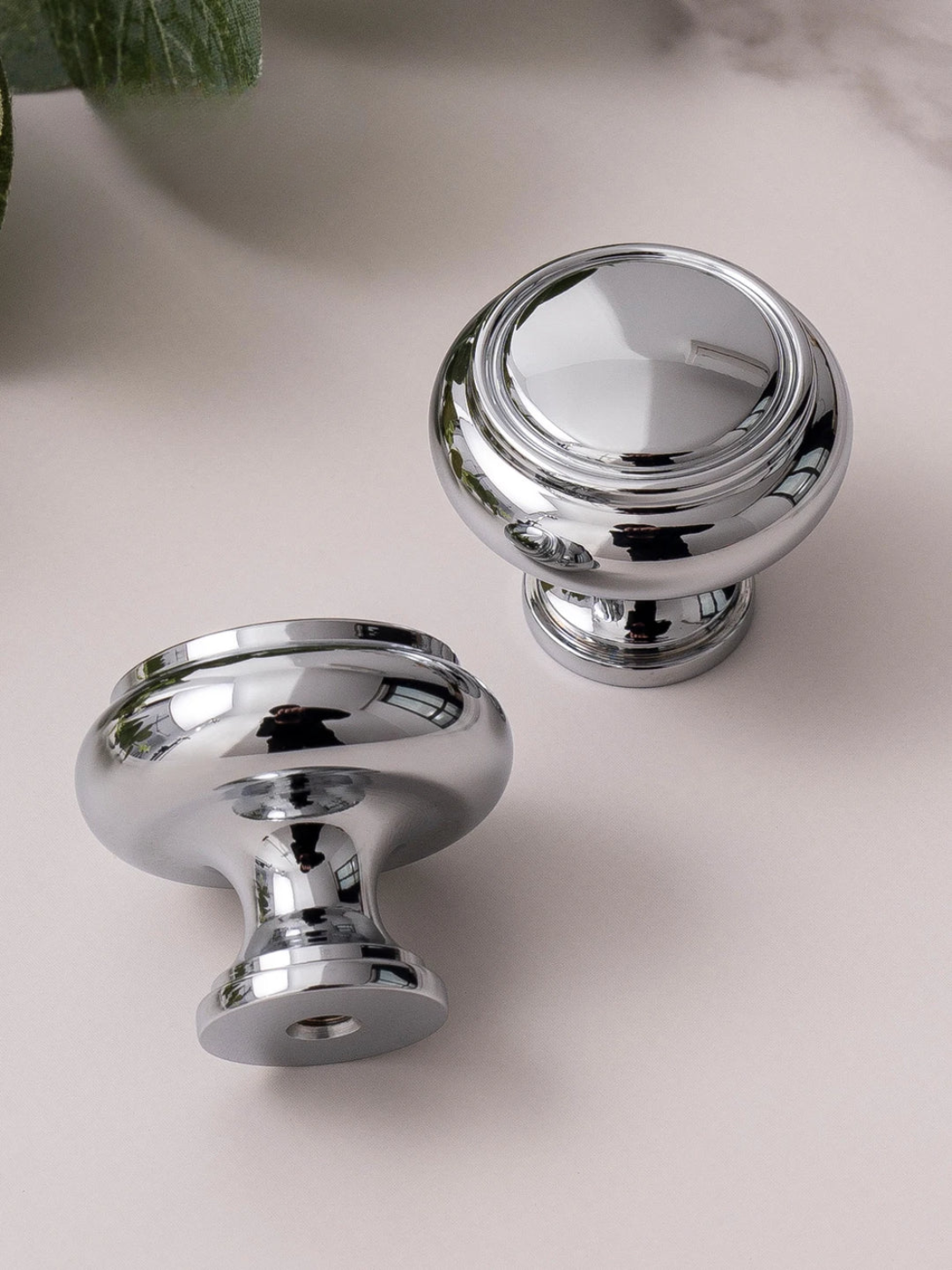 Two shiny chrome cabinet knobs on a light pink surface.
