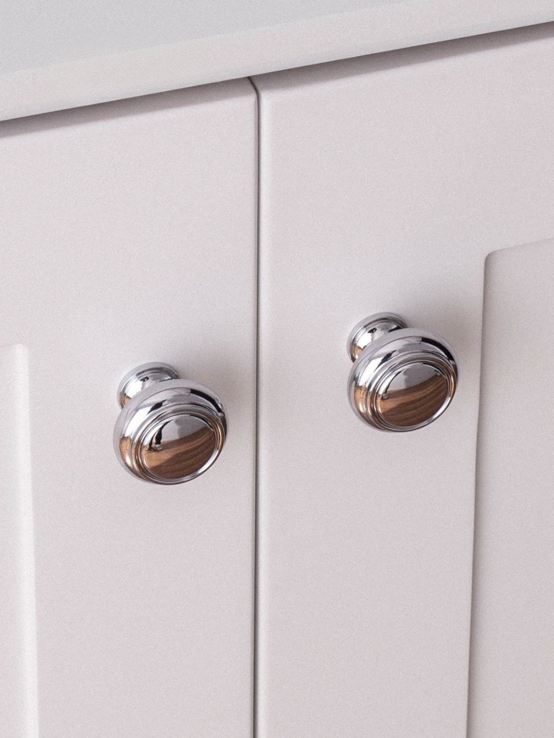 Close-up of two silver cabinet knobs on a white cabinet.